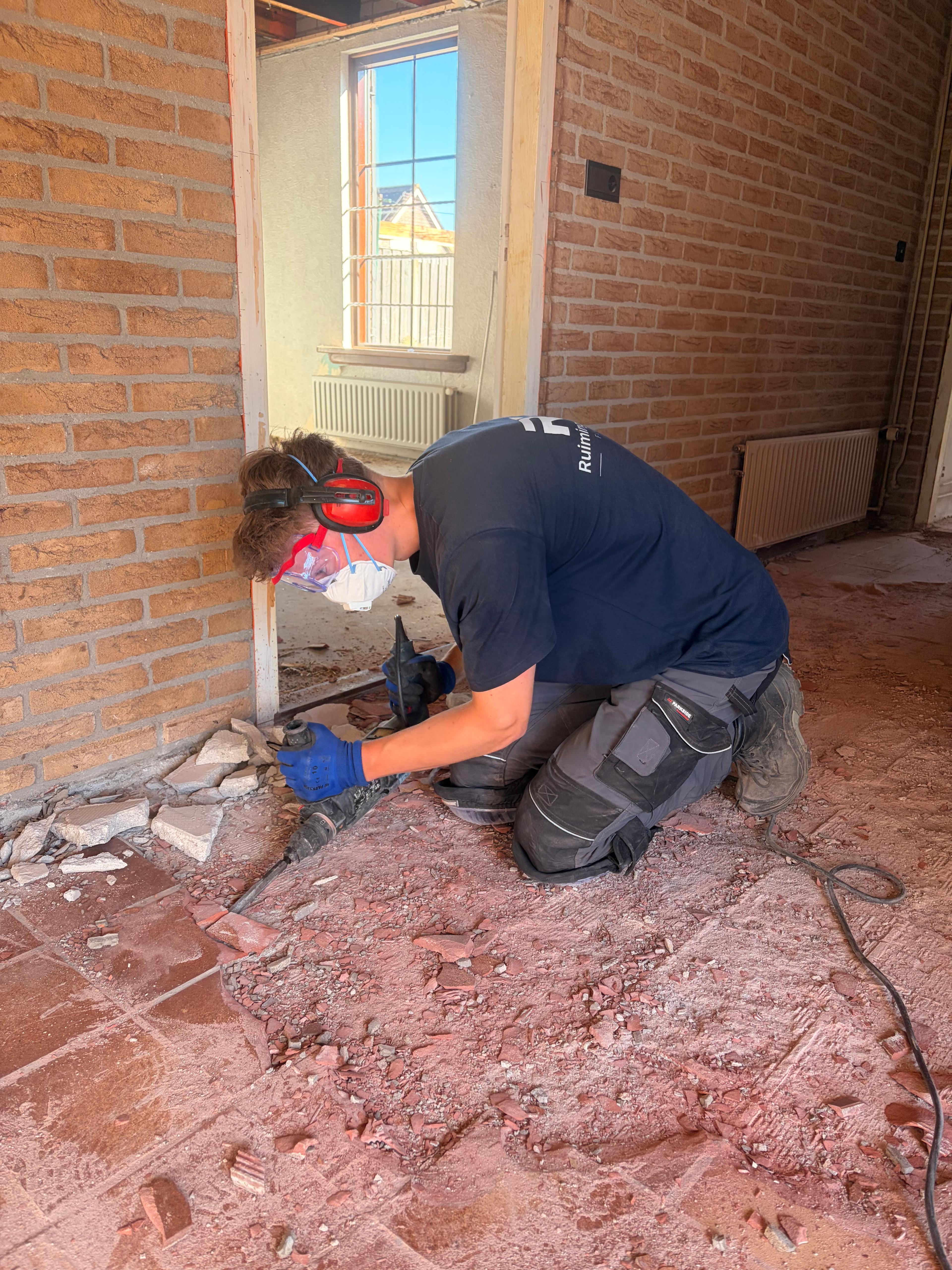 Tegelvloer wordt met een breekhamer losgehakt langs een bakstenen muur in een woning in Oosterland.